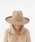 Woman wearing a tan pencil brim felt hat and a beige shirt against a plain background #color_tan