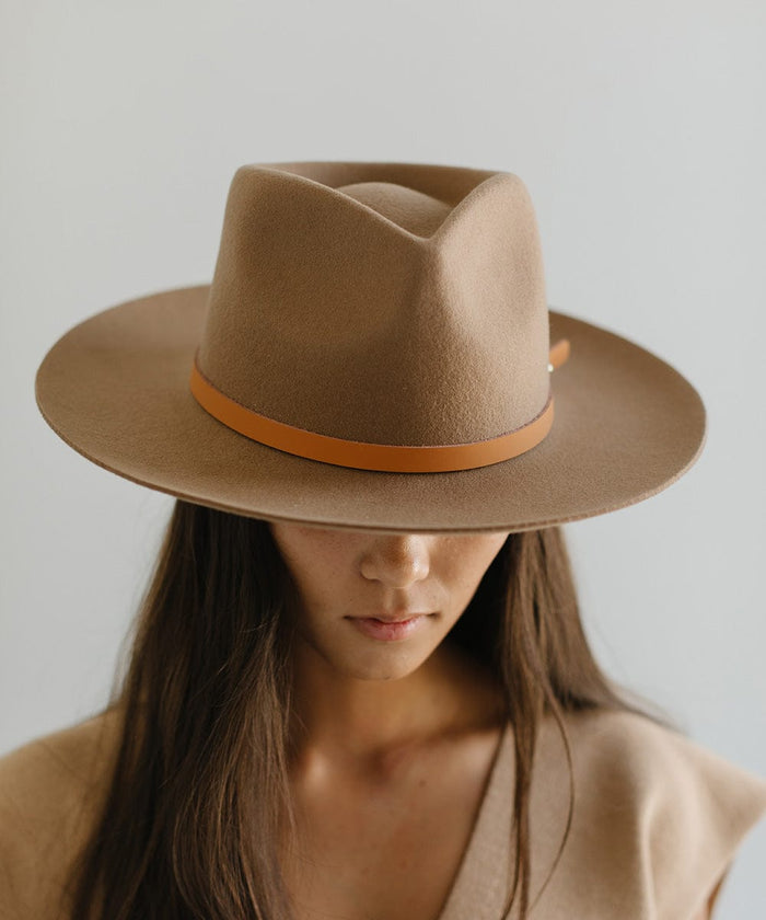Woman wearing a beige felt hat with a thin cognac leather hat band around the base against a plain background  #color_cognac