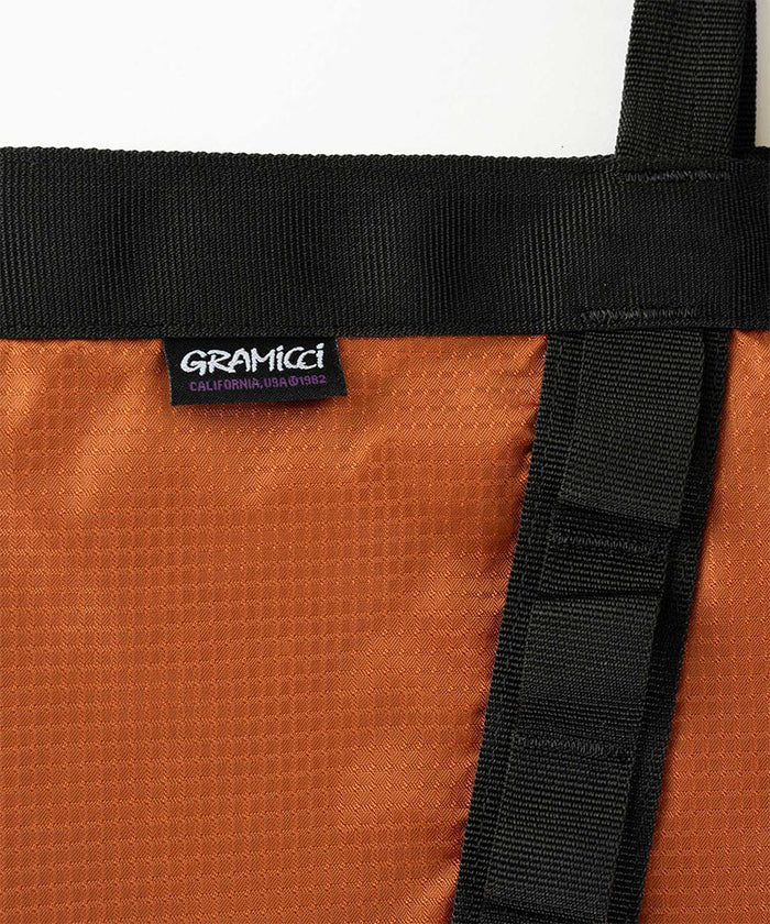 Close-up of an orange Gramicci Trail Tote bag with black straps and a Gramicci label.