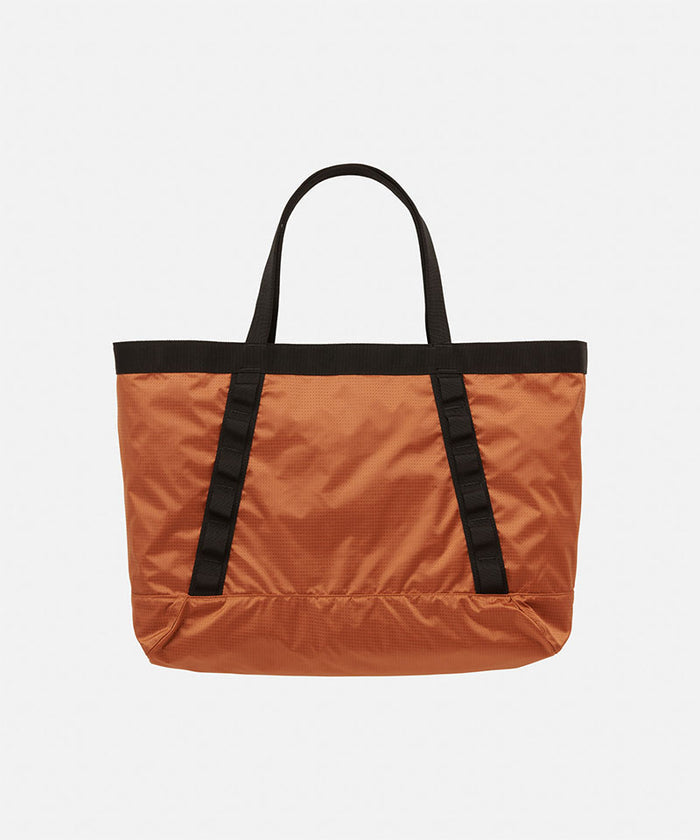 Orange Gramicci Trail Tote bag with black straps on a light tone background