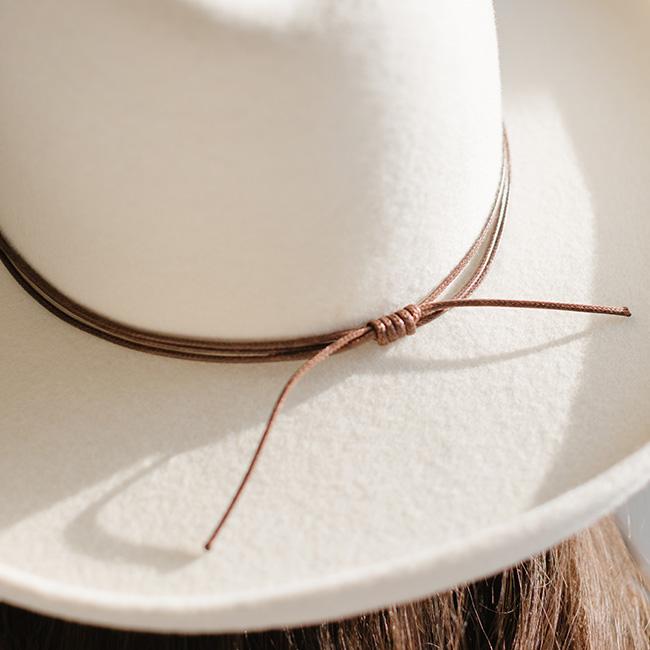 Close up image of a white cowboy hat with a brown hat band against a plain background #color_brown