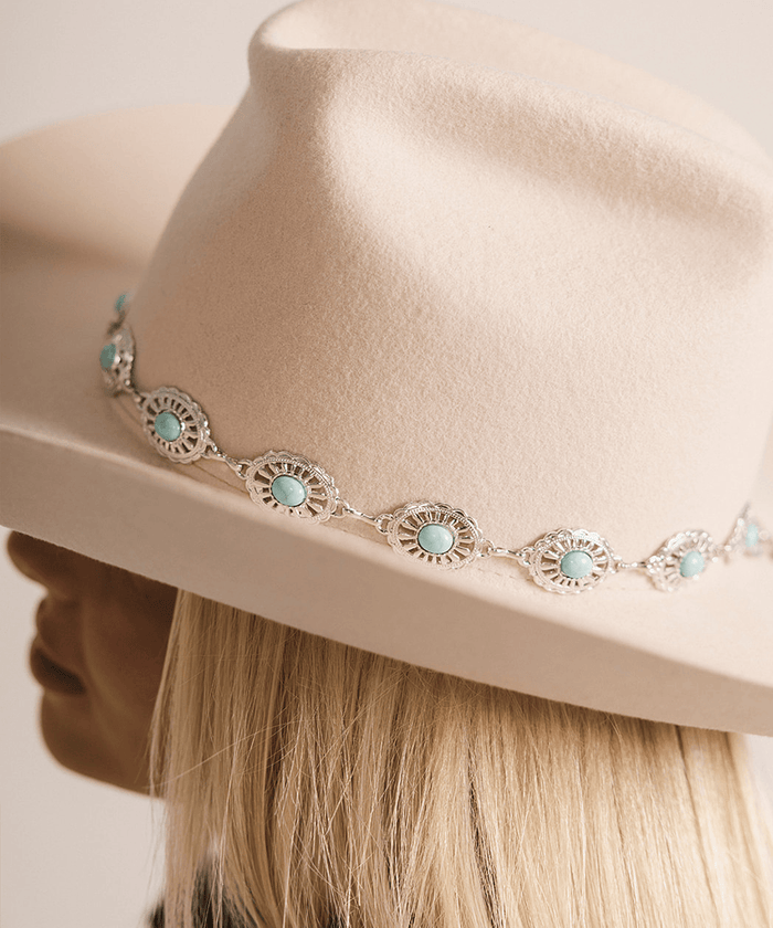 Woman wearing a white cowboy hat with a silver and turquoise concho hat band against a plain background #color_silver