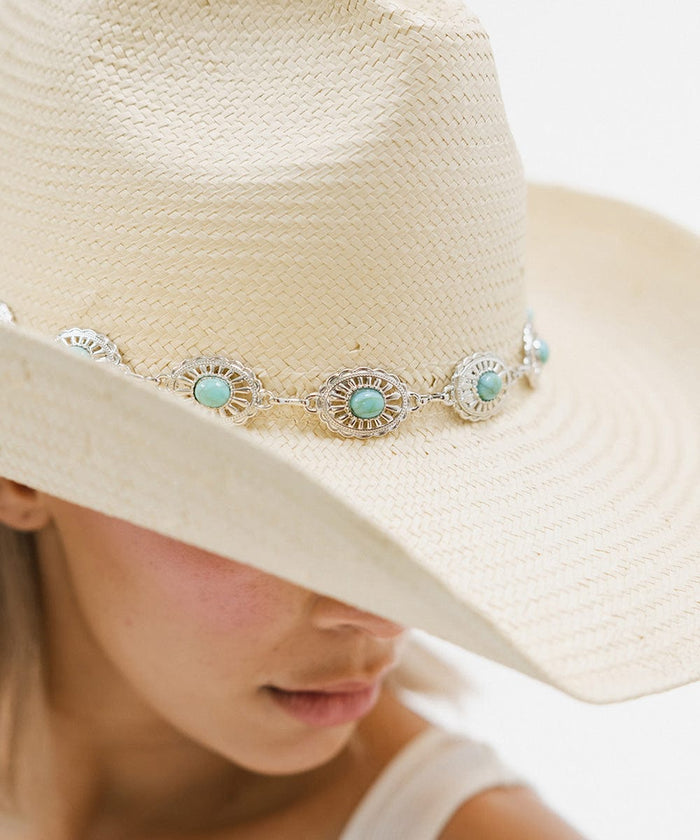 Close up image of a woman wearing a white cowboy hat with a silver and turquoise concho hat band against a plain background #color_silver