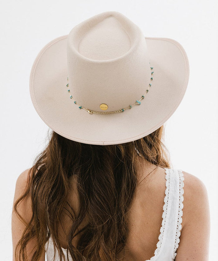 A woman wearing a cream hat with a turquoise stone hat band around the base, facing behind against a plain background #color_gold