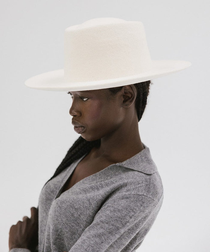 Woman wearing an off white gambler hat and a grey shirt, facing sideways  against a plain background #color_off white