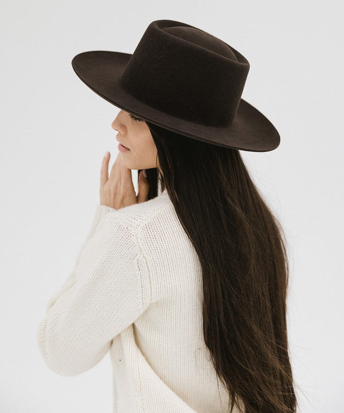Woman with long hair wearing a dark brown gambler hat and a white sweater, facing sideways against a plain background #color_dark brown