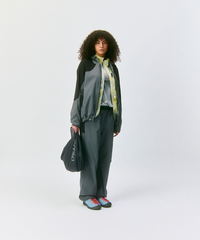 Model wearing a grey and black jacket and grey pants holding an olive Gramicci Ultra-Light Shopper on a light-tone background.