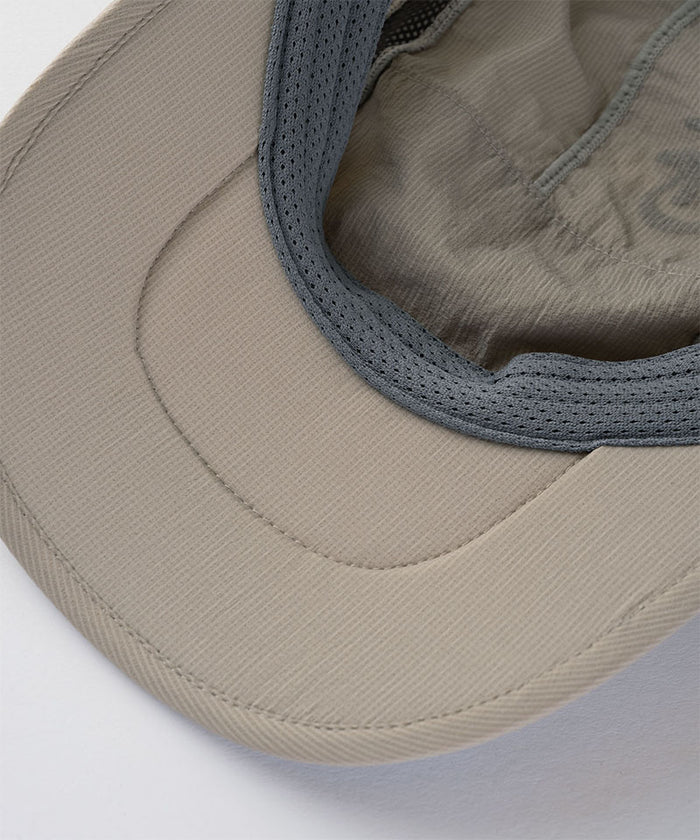 Close-up of a concrete beige colored Gramicci Ultra-Light Tech Cap with a gray mesh band on a light tone background