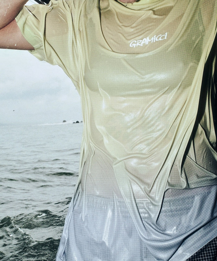 Person wearing a light-colored wet shirt with 'Garmicci' branding by the water.