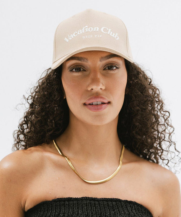 Woman wearing a tan cap with 'Vacation Club' text and a gold chain against a plain background  #color_tan
