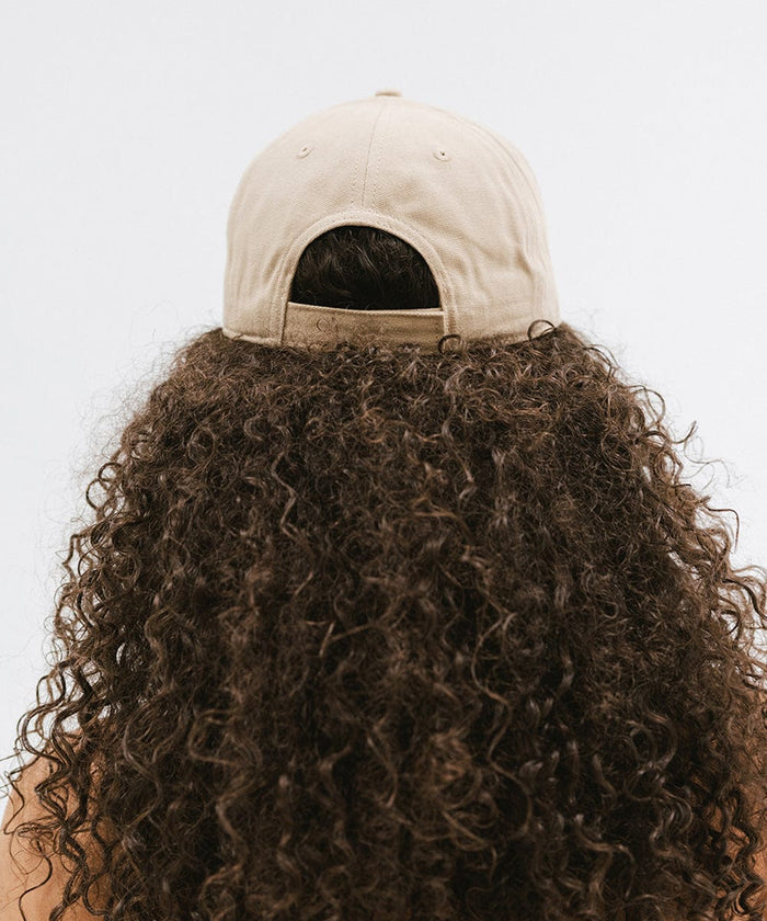Woman with curly hair wearing a tan cap against a plain background  #color_tan