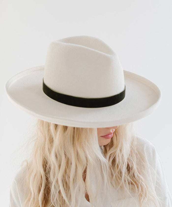 Woman wearing a white hat with a forest green velvet chain hat band against a plain background #color_forest green