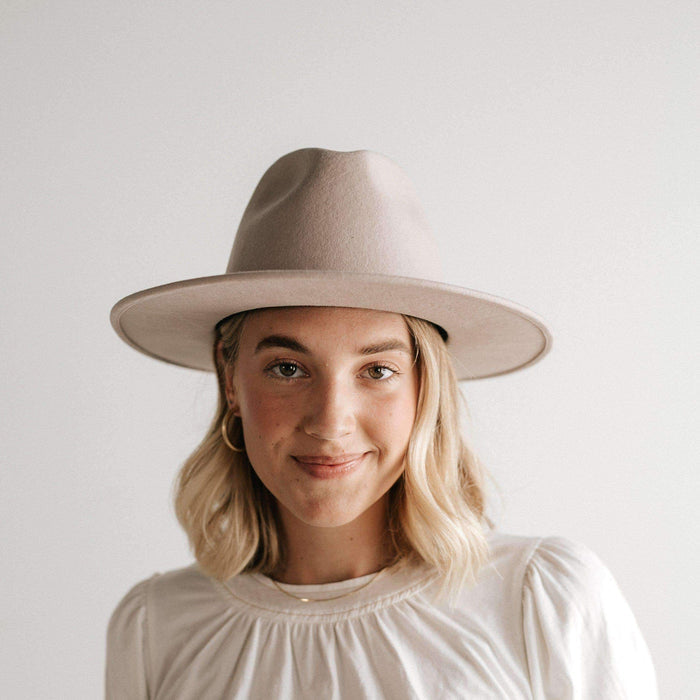Woman wearing an ivory colored fedora hat and a white top against a plain background #color_ivory