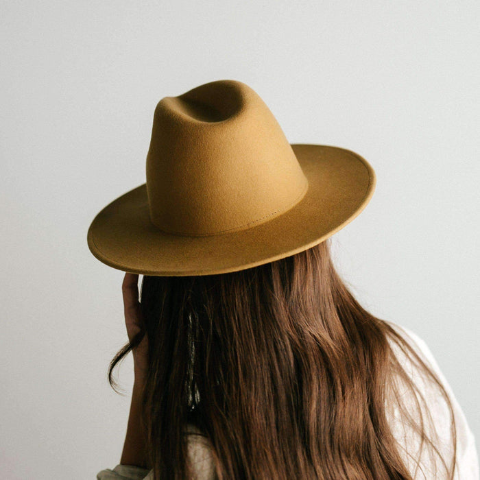 Woman wearing a mustard colored fedora hat facing behind against a plain background #color_mustard