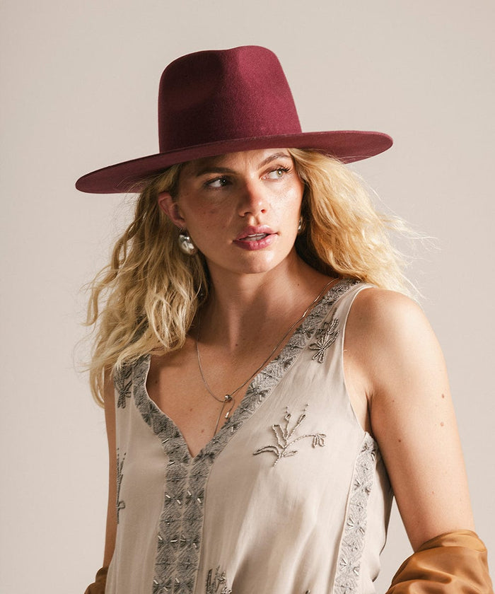Woman wearing a merlot fedora hat and beige embroidered top against a plain background #color_merlot