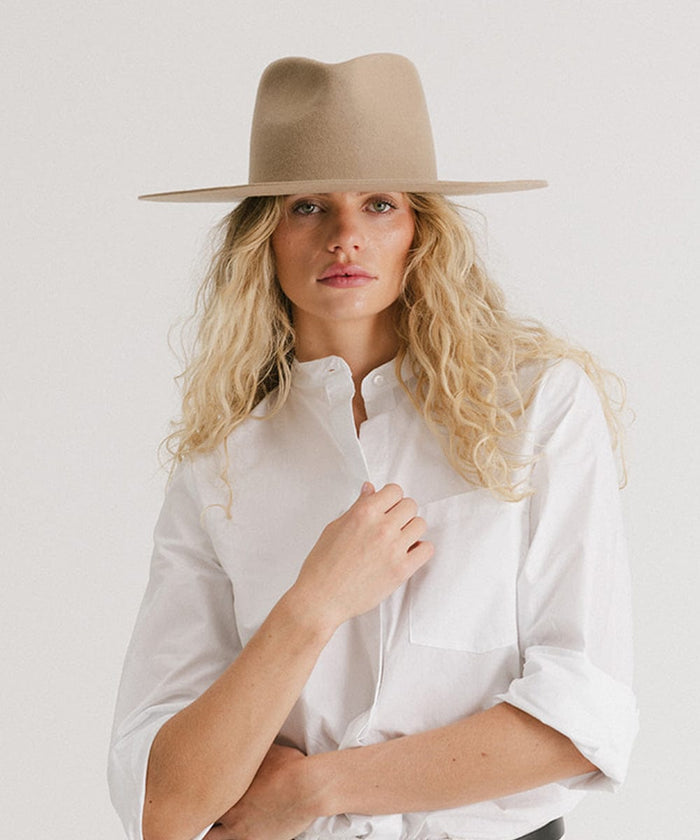 Woman wearing a tan fedora hat and a white shirt against a plain background  #color_tan