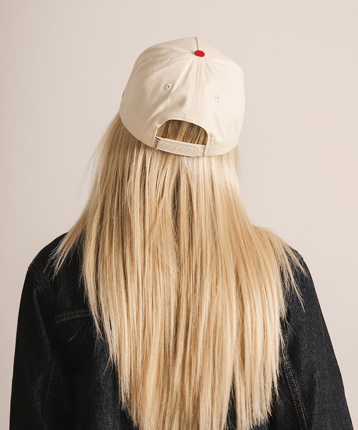 Person with long blonde hair wearing a beige cap on a plain background #color_cream - red