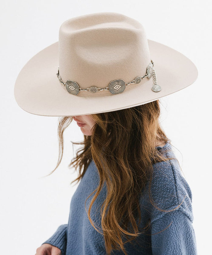 Woman wearing a cream hat with a silver western concho band and a blue sweatshirt, looking sideways against a plain background #color_silver