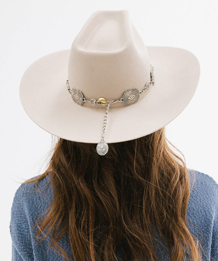 Woman wearing a cream hat with a silver western concho band and a blue sweatshirt, facing behind against a plain background #color_silver