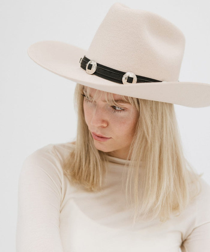 A woman wearing a white hat with a black western style genuine leather hat band and a white top against a plain background #color_black