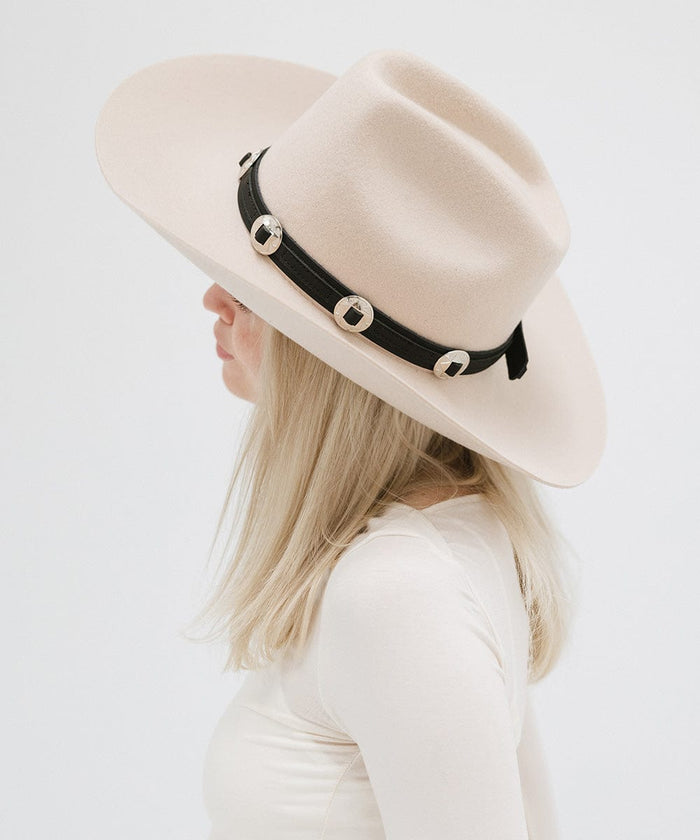 A woman wearing a white hat with a black western style genuine leather hat band and a white top, facing sideways against a plain background #color_black