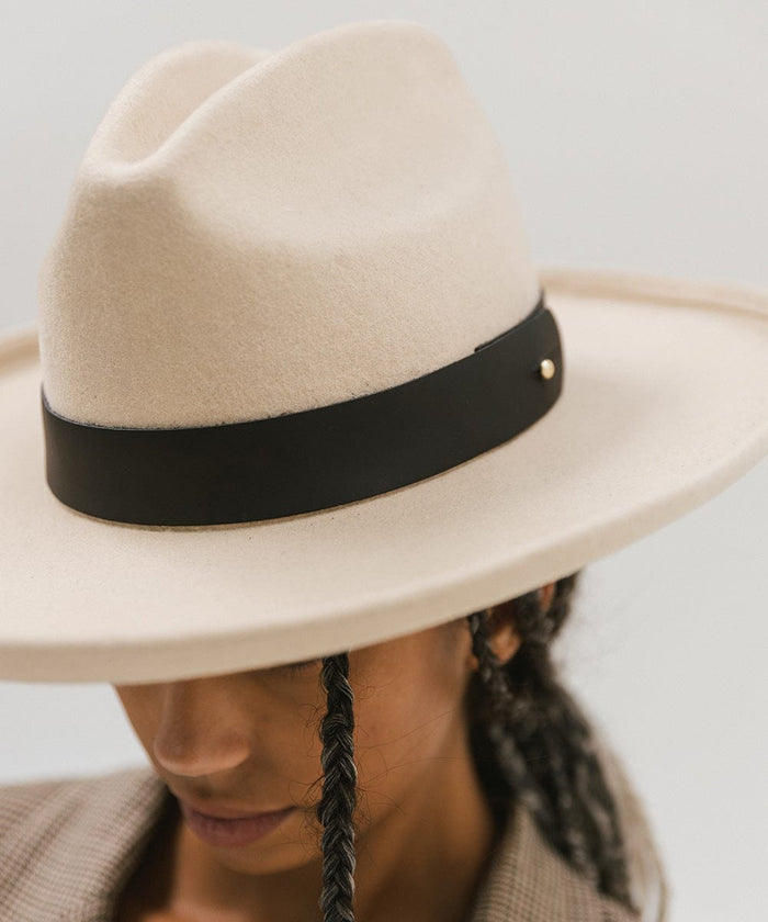 Woman wearing a cream hat with a wide black leather band around the base against a plain background #color_black
