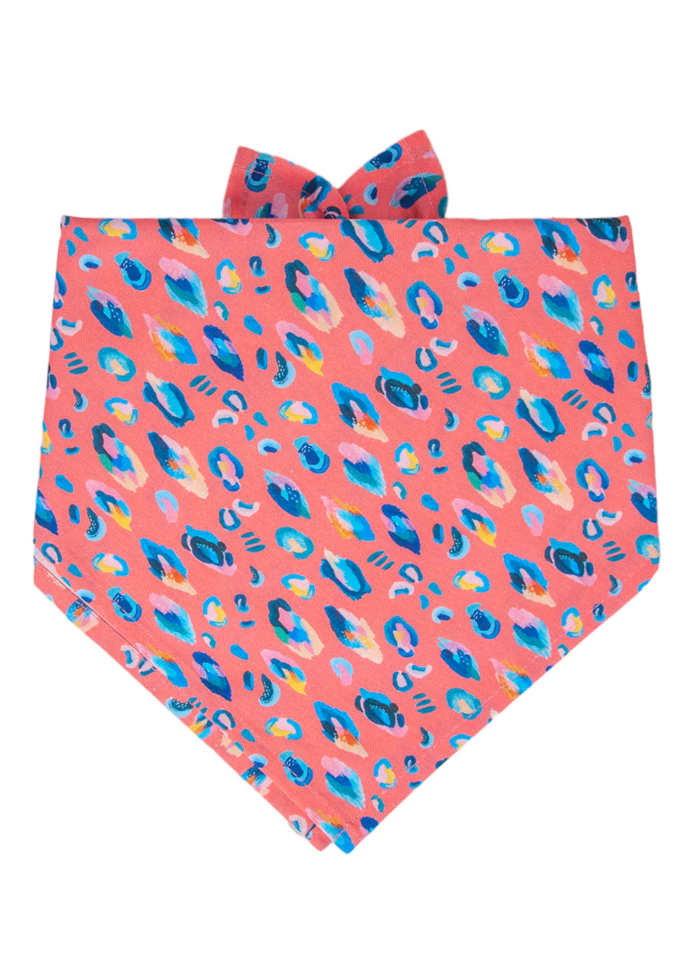 A bold tie-on dog bandana with a coral pink base and painterly leopard spots in  — the ultimate statement accessory.
