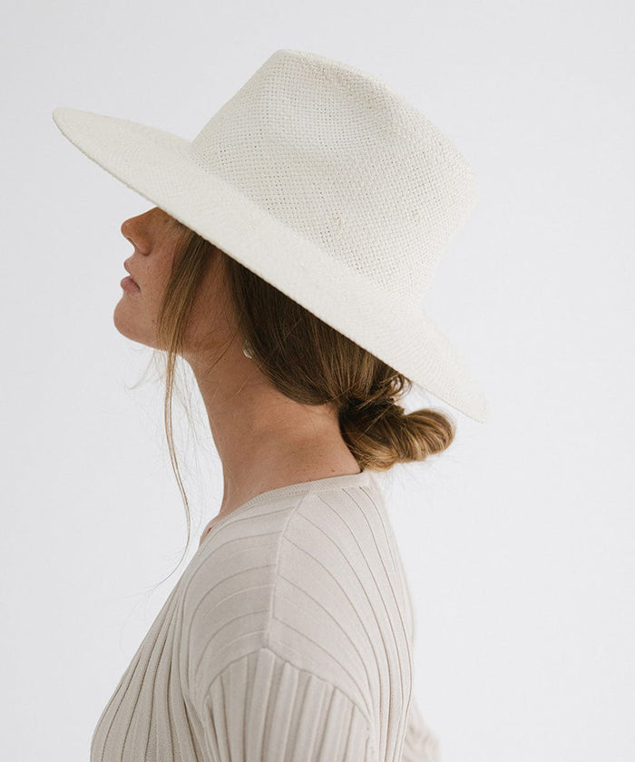 Woman wearing a white wide brim fedora straw hat and a grey top, facing sideways against a plain background  #color_white