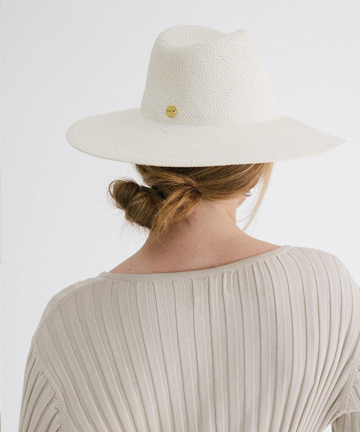 Person wearing a white wide brim fedora straw hat with a gold pin and a grey top, facing behind against a plain background  #color_white