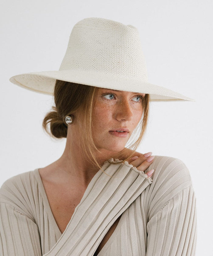 Woman wearing a white wide brim fedora straw hat and a grey top, posing against a plain background  #color_white