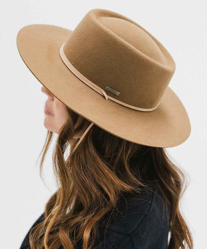 Woman wearing a brown hat with a hat band and a dark blue sweater, facing sideways against a white background #color_brown
