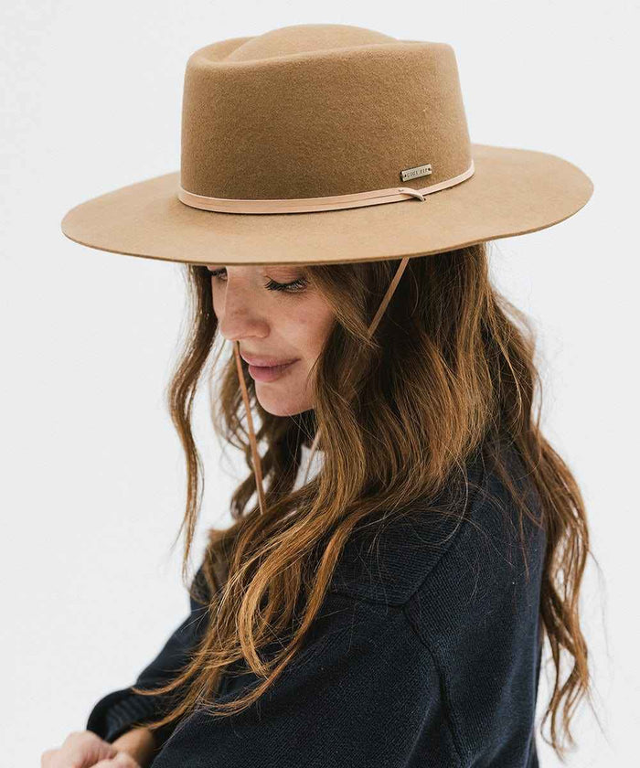 Woman wearing a brown hat with a hat band and a dark blue sweater, looking down against a white background #color_brown