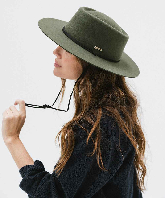 Woman wearing a green fedora hat with a hat band and a dark blue sweater, facing sideways against a plain background #color_green