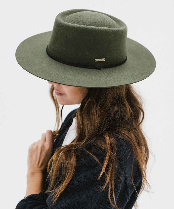 Woman wearing a green fedora hat with a hat band and a dark blue sweater, posing sideways against a plain background #color_green