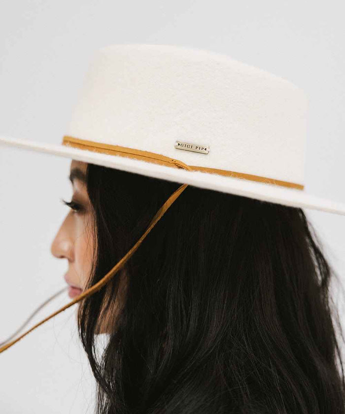 Close up image of a woman wearing an off white wide-brimmed hat with a strap, facing sideways against a plain background #color_off white