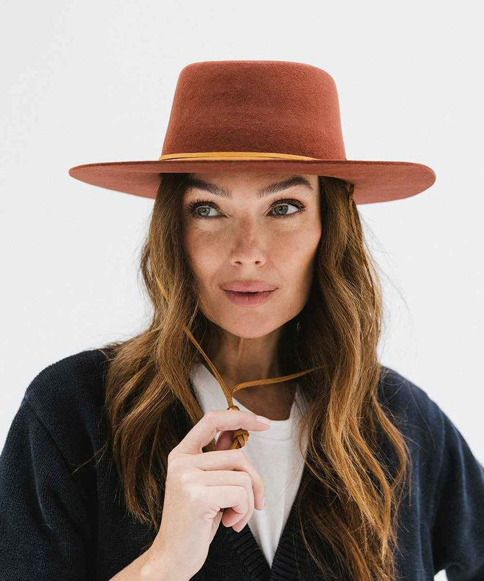 Woman wearing a rusty red colored hat and a dark blue shirt against a white background #color_rusty red