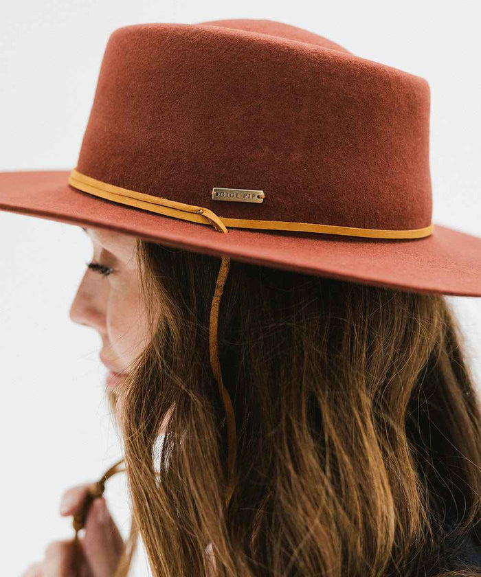 Rusty red colored hat with a yellow band worn by a woman on a white background #color_rusty red