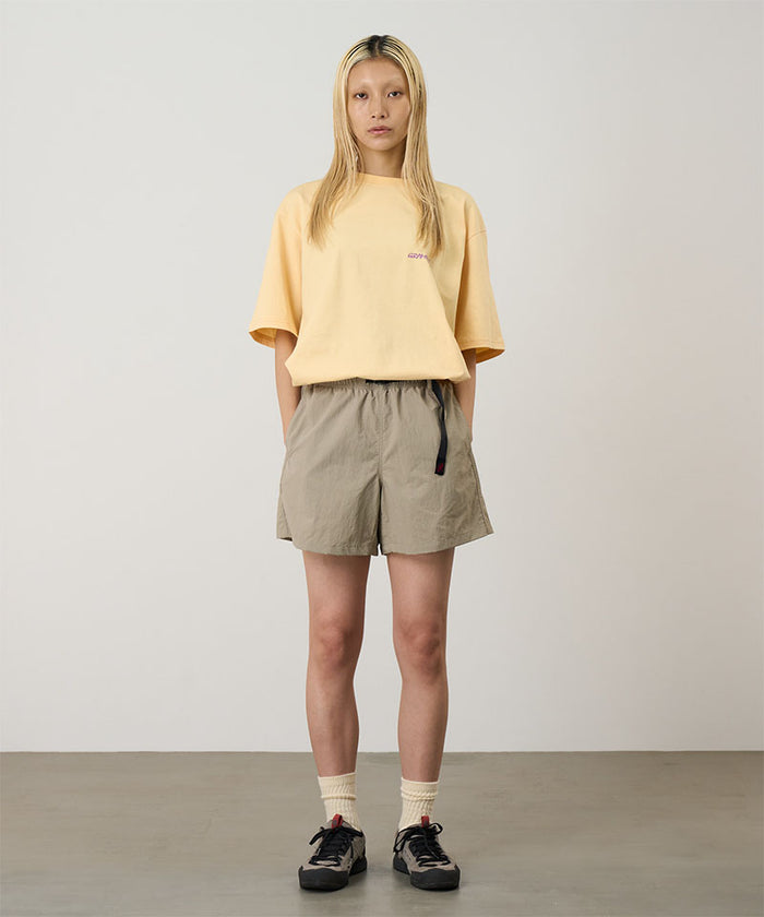 Model wearing milk tea Gramicci Women's Nylon Active Short and a yellow shirt on a light-tone background.