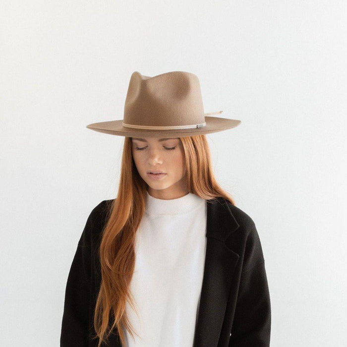 Woman wearing a brown fedora hat with a hat band and a white t-shirt with a black blazer against a plain background #color_brown