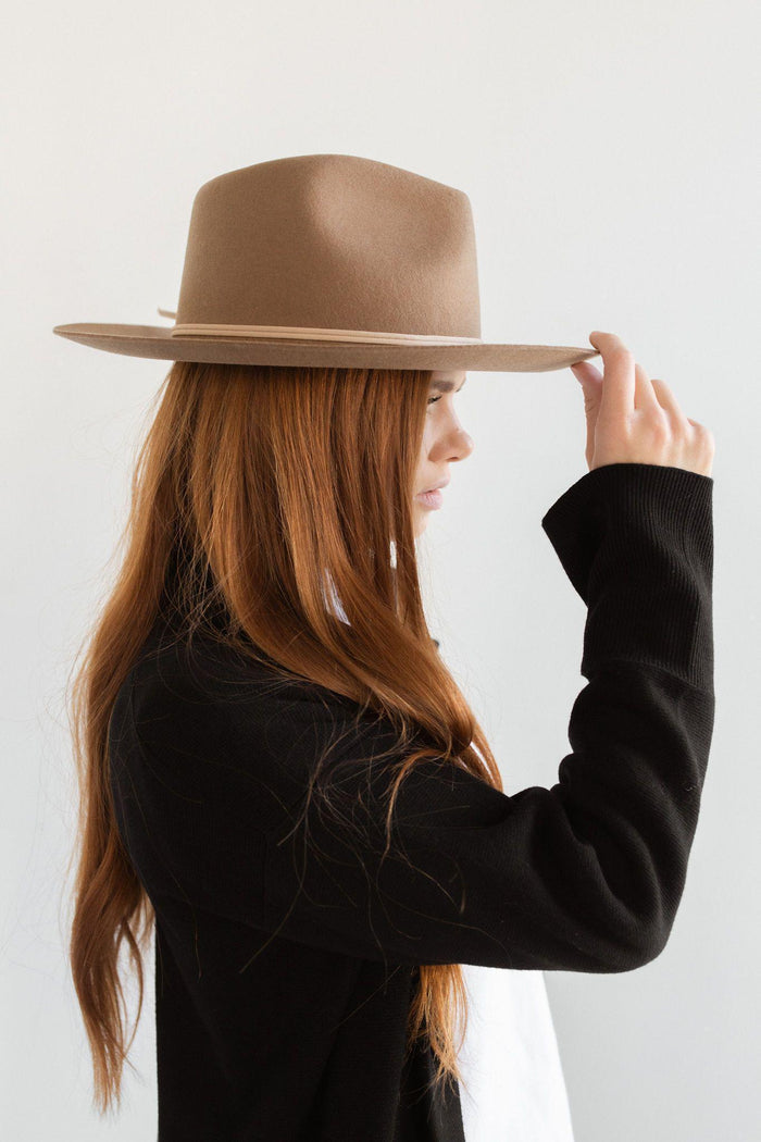 Woman wearing a brown fedora hat with a hat band and a white t-shirt with a black blazer, facing sideways against a plain background #color_brown
