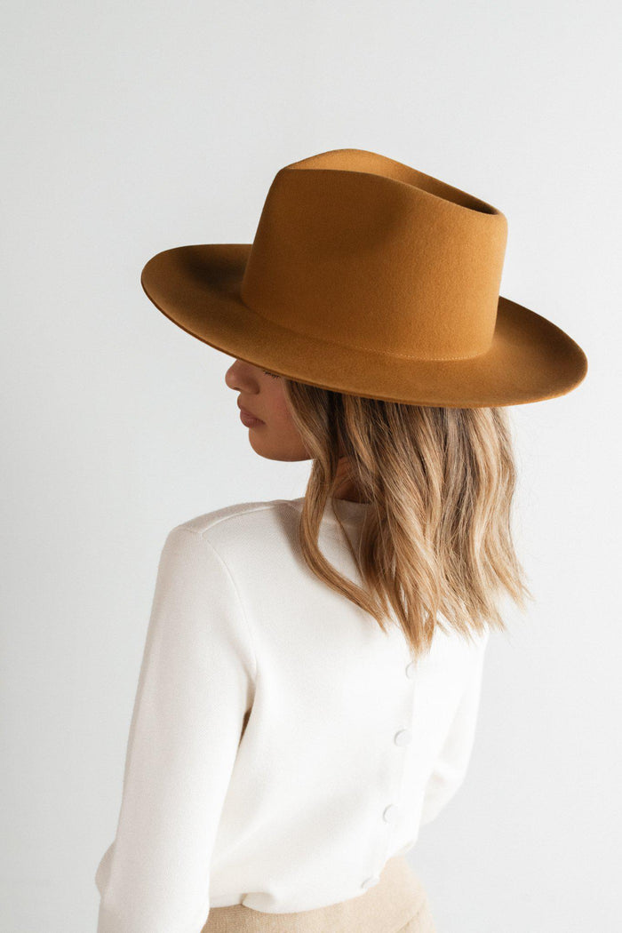 Woman wearing a cinnamon colored fedora hat and a white shirt, facing sideways against a plain background #color_cinnamon