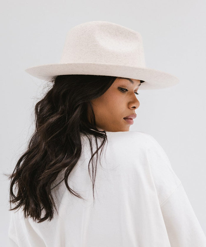 Woman wearing a mix ivory colored fedora hat and a white shirt, looking sideways against a white background #color_mix ivory