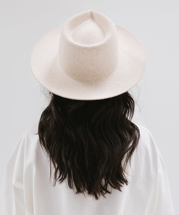 Woman wearing a mix ivory colored fedora hat and a white shirt, facing behind against a white background #color_mix ivory