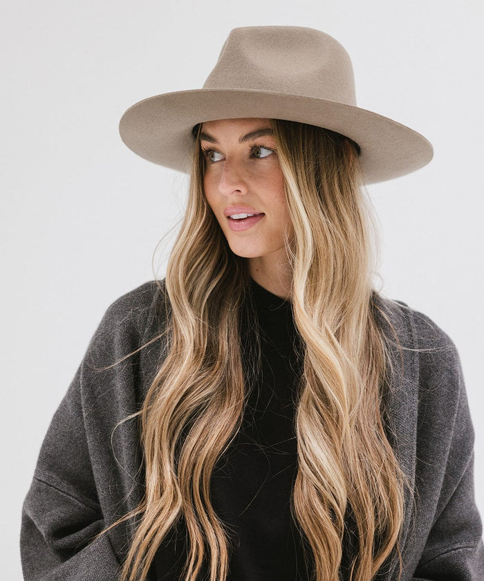 Woman wearing a sage fedora hat and a black top with a dark grey jacket, looking sideways against a white background #color_sage