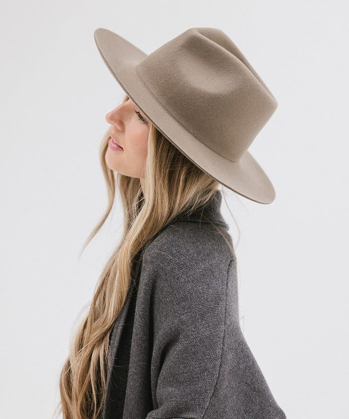 Woman wearing a sage fedora hat and a dark grey jacket, facing sideways against a white background #color_sage