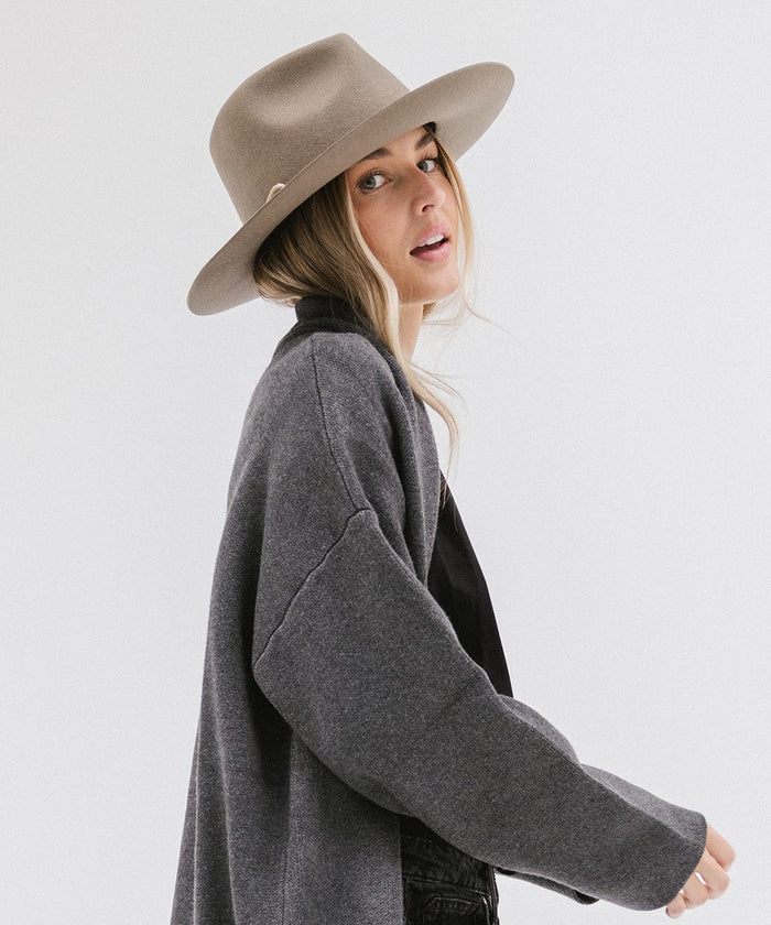 Woman wearing a sage fedora hat and a dark grey jacket, posing against a white background #color_sage