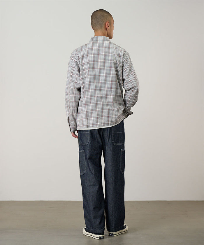 Model wearing a natural shadow plaid Gramicci Zip-Up Garage Jacket and dark blue pants on a light-tone background.